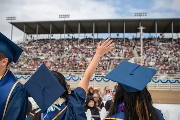 An alumni in cap and gown waves at the crowd