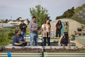 Students with academic and career advisor Selena Plancarte - Arizmendi in front of a garden bed of samples taking notes