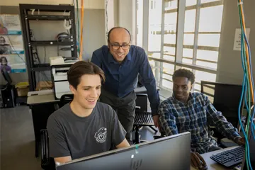 Two students working while their professor oversees them in the business and information technology building
