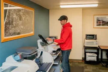 Mail services staff at ���ӽ紫ý processes and scans packages using automated sorting equipment, with aerial campus maps displayed on the wall.