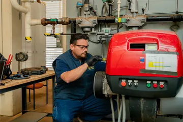 A facilities worker calibrates and adjusts a red industrial machine, part of the university’s heating and utility system infrastructure.
