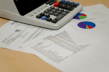 A tabletop view of printed financial documents and colorful pie charts beneath a calculator during budget review at �鶹��’s Finance Department.