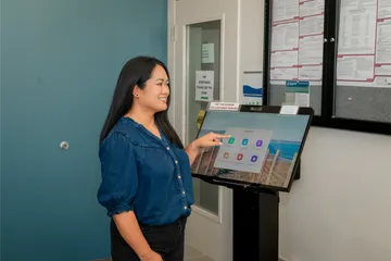 An employee interacts with a digital HR kiosk at ���ӽ紫ý, smiling while selecting options on the touchscreen labeled “Welcome to ���ӽ紫ý HR.”