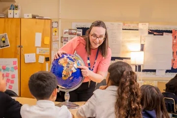 Student worker pointing at a globe and talking to students.