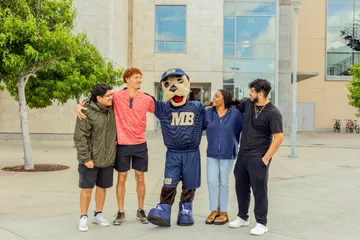 Students standing with the Mascot in front of the building