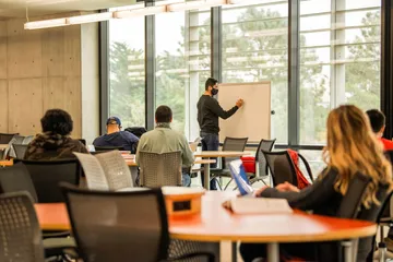 Instructor writing on a whiteboard while students listen in a classroom.