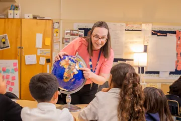 A teacher points to a location on a globe while his students look on.