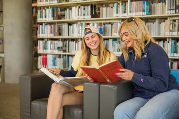 Two girls sitting on sofa and similing and reading the book together