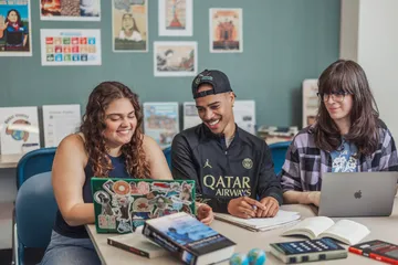 Three people pose for a photo while looking at a laptop.