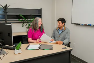 A CSUMB finance team member meets one-on-one with a student in a welcoming office space, smiling and reviewing documents across the desk.