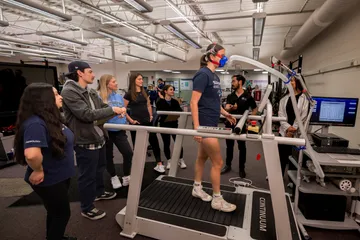 A girl is using the treadmill surrounded by a bunch of people