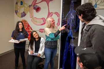A professor giving a presentation to a group of students using a digital anatomy board and everyone is smiling