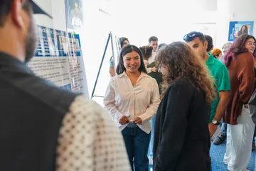 A student presenter smiles at an onlooker in the audience during her presentation
