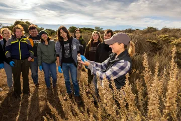 Students group up in front of a professor to see her holding up a field mouse.