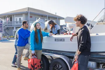 A group of four students standing next to a boat