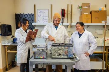 Students in lab coats observe and take notes while conducting a tank experiment in a marine science lab