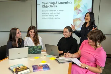 Four students sitting at a table listening to their professor teach them.