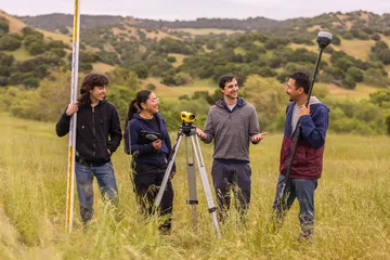A group of four AES students holding surveying tools while collaborating together