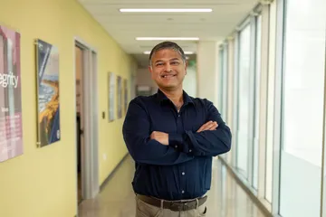 A masters of business administration professor smiling at the camera with their arms crossed