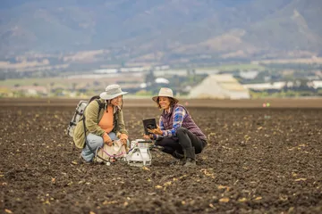 Two people leaning down together in a field doing field work.