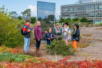 CSUMB environmental science students take notes while listening to faculty during an outdoor field lesson in a coastal habitat.
