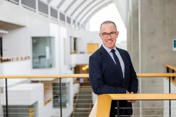 CSUMB Provost Andrew Lawson stands by a railing inside a modern campus building.