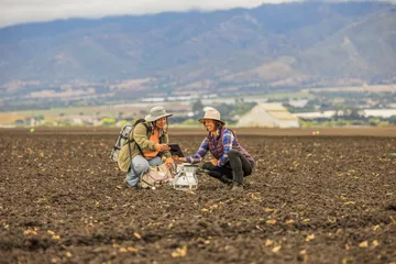 Two people leaning down together in a field talking.
