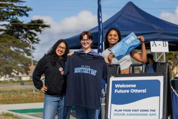 Three students posing for a picture with college merchandise