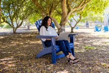 A masters of business administration professor sitting down on a chair working on their laptop outside