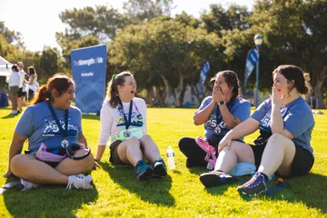 4 participants of MB madness sit together in a circle in the grass and laugh