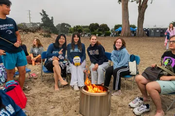 Students sitting around fire on a beach