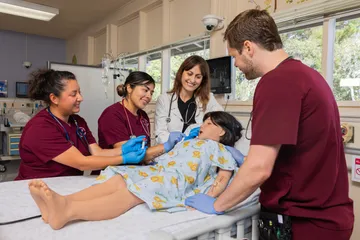 Nursing student and teacher around a hospital bed with mannequin