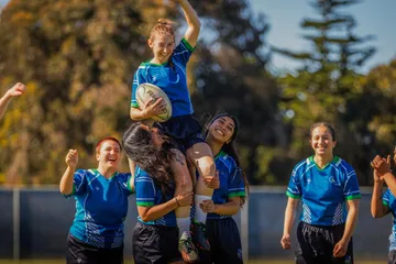 Womens rugby team celebrating, holding one player up on shoulders
