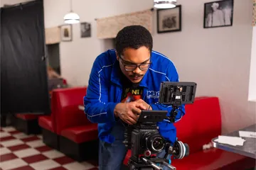 Film crew member bent down looking at the camera being used for filming