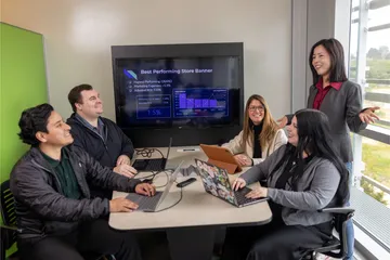 A business administration professor giving a presentation to a group of four students