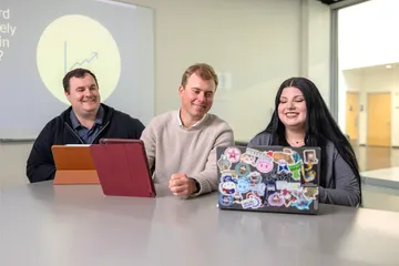 A group of three business administration students sitting down collaborating together