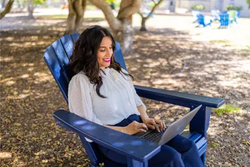 A masters of business administration professor sitting down on a chair working on their laptop outside