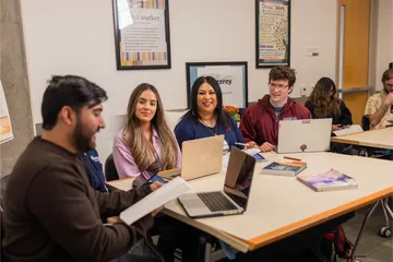 A group of five social work credential students sitting down at a table listening to one talk
