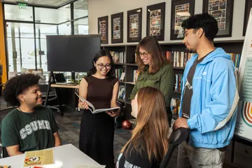 A group of students standing and sitting while a professor stands with them and a student holds open a book smiling