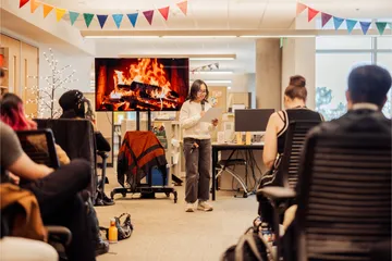 A student standing, reading from a paper and holding a mic while she presents to a group of attendees sitting down.