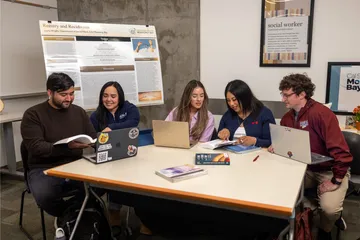 A group of five social work credential students sitting down at a table and collaborating together