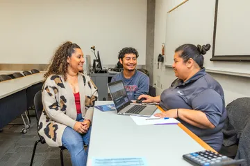Faculty member having a conversation with a student and their family member at a table with a computer.