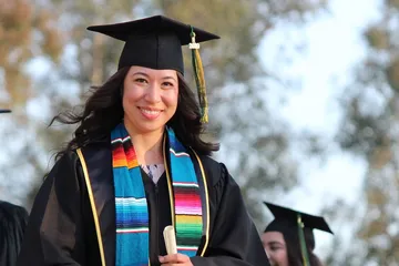 woman wearing regalia holding a diploma