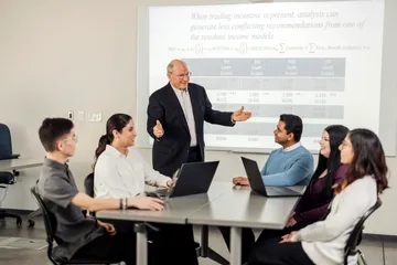 The teacher, wearing a black blazer, is teaching the students.