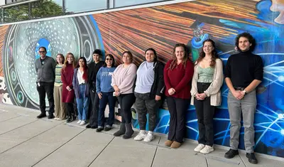Student award winners shown lining up in front of a mural