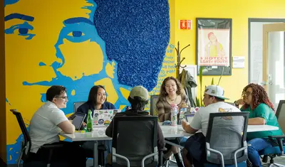 Diverse group of students at table with mural behind it