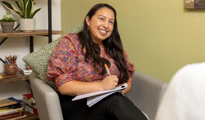 Woman sitting on couch, writing in a notebook while smiling