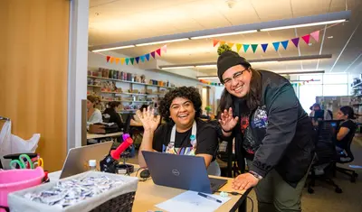 Students smiling and waving in the maker space