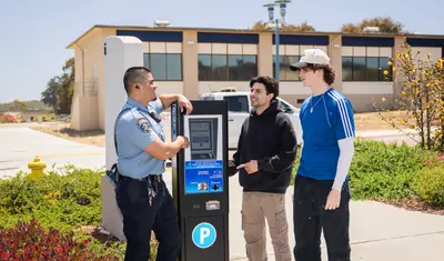 A parking service officer assisting two students with a terminal