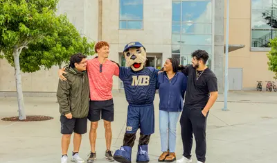 Students standing with the Mascot in front of the building